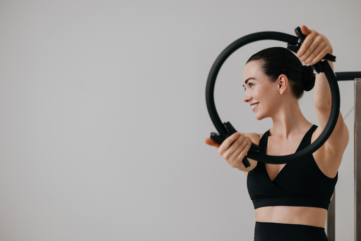 Smiling young woman holding a pilates ring in hands while doing pilates training. Fitness workout with pilates circle for strength and balance